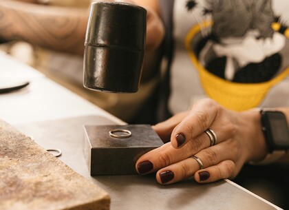 En person håller en ring på ett städ och slår med en hammare, troligen vid smyckestillverkning.