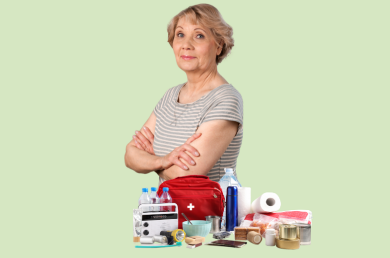 Äldre kvinna med armarna i kors står framför nödutrustning som vatten, konserver och första hjälpen-kit.