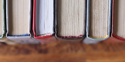 Böcker stående på rad, fotograferade ovanifrån med fokus på bokryggarna och träbordet under.