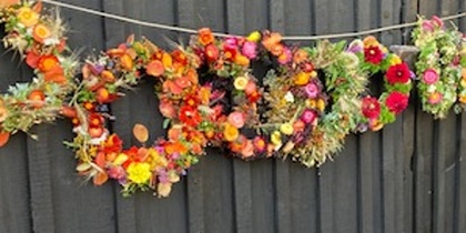 Flera färgglada blomkransar hänger på ett snöre framför en svart träport utomhus.