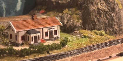 Modelljärnväg med ett litet hus, järnvägsspår och berg i bakgrunden.