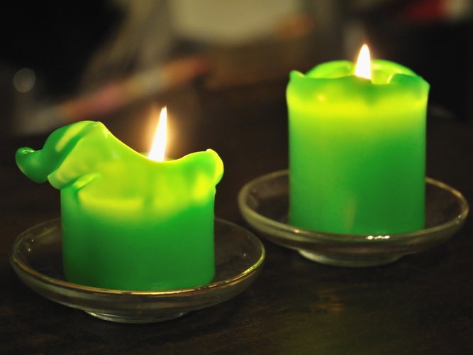 Två gröna stearinljus brinner på små glasfat på ett mörkt bord.