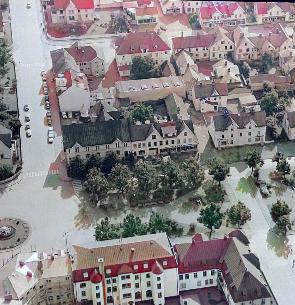 Flygfoto över en liten stad med röda och vita hustak, träd och gator.
