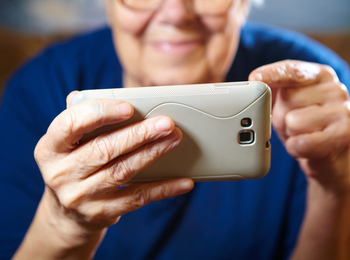 En äldre person håller en smartphone med båda händer och använder pekfingret på skärmen.