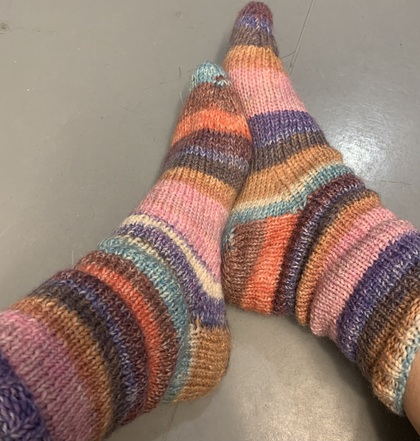 Två fötter med stickade, färgglada randiga sockor på ett grått golv.