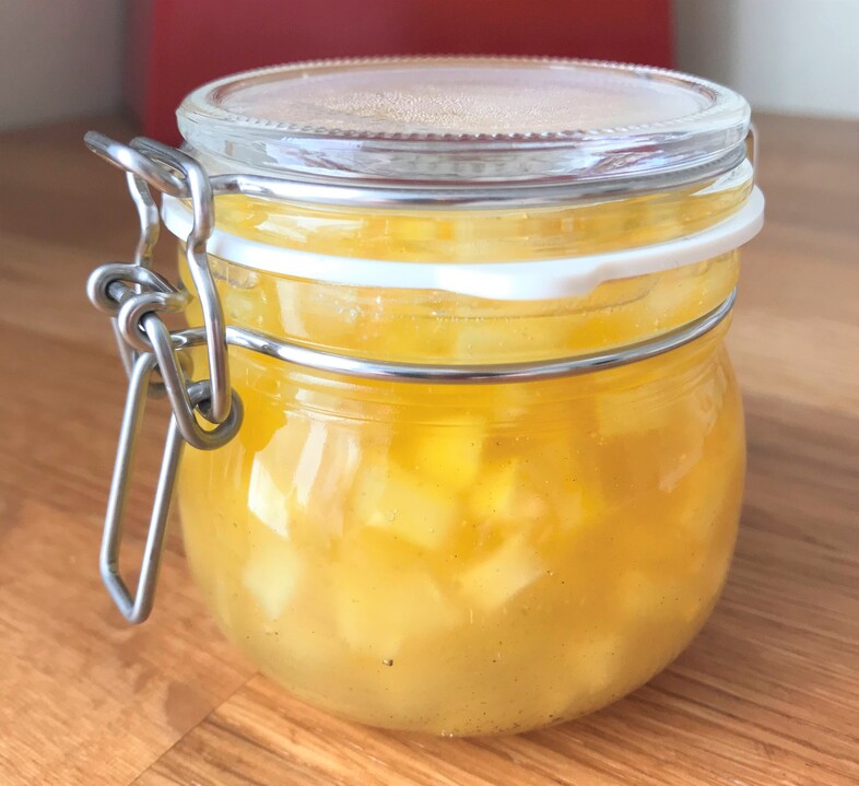 En glasburk med tättslutande lock fylld med gul fruktkompott står på ett träbord.