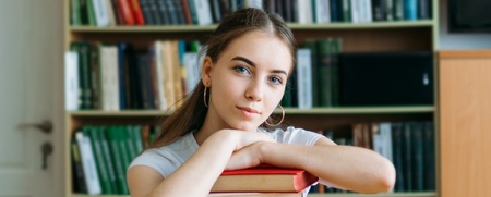 En ung kvinna sitter vid ett bord i ett bibliotek med en hög böcker framför sig.