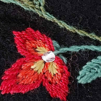 Närbild av en broderad röd och gul blomma med grön stjälk på svart tyg.