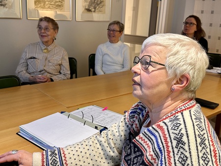 Fyra äldre kvinnor sitter vid ett konferensbord, en med anteckningsblock framför sig.