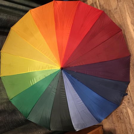 Ett paraply med sektioner i regnbågens alla färger ligger uppfällt på ett trägolv.