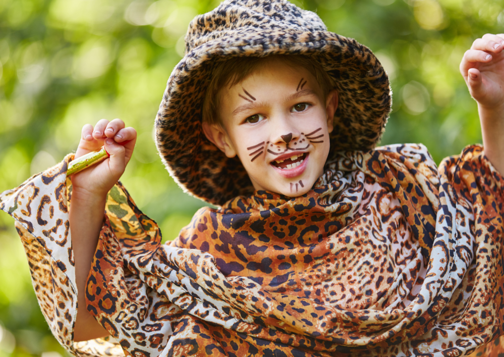 Barn utklätt till leopard med ansiktsmålning och djurmönstrade kläder, poserar lekfullt utomhus.