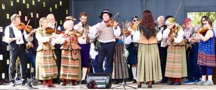 En grupp musiker i folkdräkter spelar instrument på en scen utomhus.