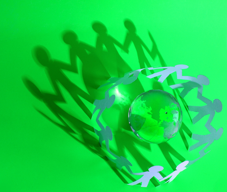 Pappersfigurer i ring runt en glaskula med jordglobsmotiv, starkt grön bakgrund.