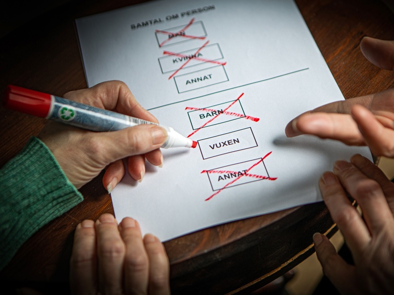 Två händer markerar och kryssar i rutor på ett formulär med en röd penna.