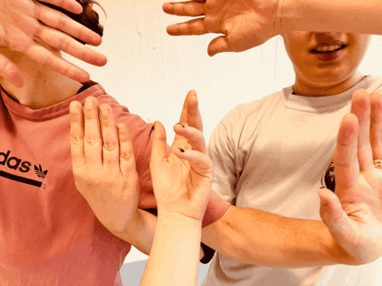 Två personer håller upp händerna framför sig i olika gester mot en ljus bakgrund.