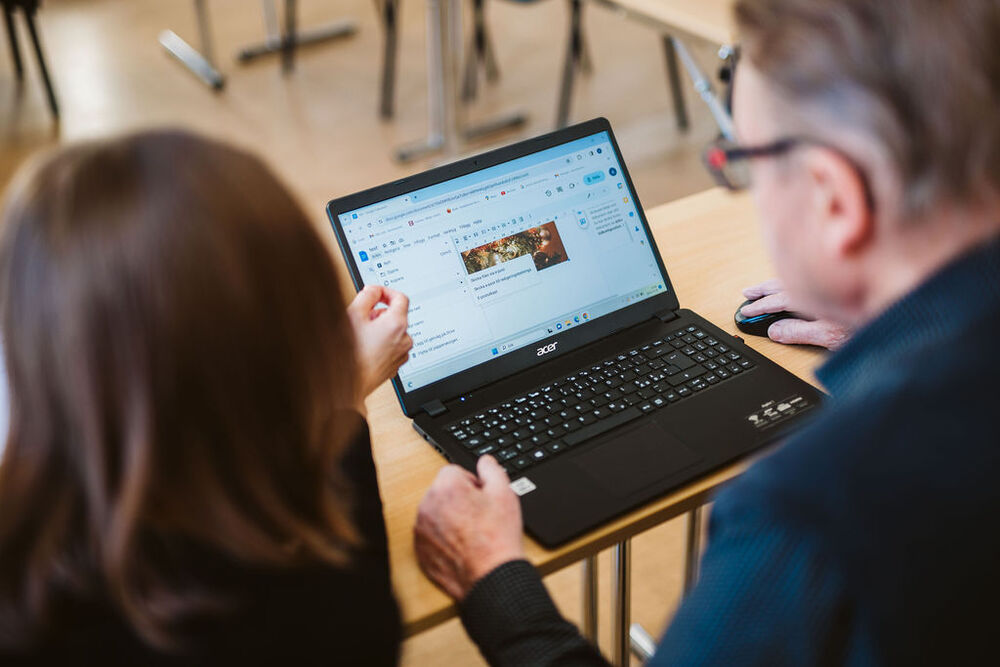 Två personer sitter vid ett bord och tittar på en bärbar dator tillsammans.