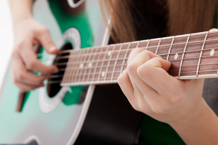 Närbild av en person som spelar på en grön akustisk gitarr, fokus på händer och gitarrhals.