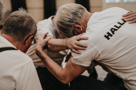 Flera äldre personer sitter i en cirkel och håller varandras armar i en stödjande gest.
