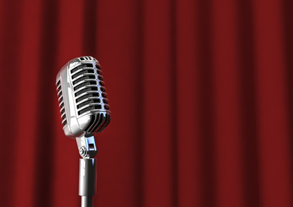 En klassisk mikrofon står framför en röd sammetsgardin, redo för ett framträdande eller tal.