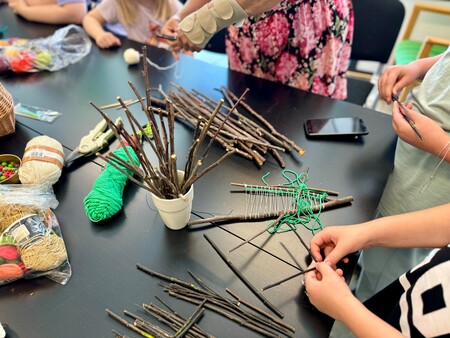 Barn pysslar med pinnar, garn och snöre vid ett bord under en hantverksaktivitet.