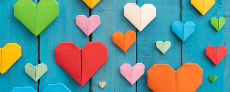 Flera färgglada origamihjärtan i olika storlekar på en blå träbakgrund.