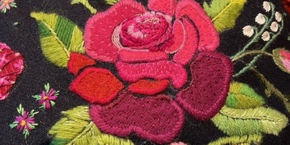 Närbild av broderad ros och blommor i starka färger på mörkt tyg.