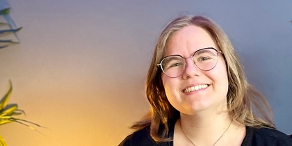Två leende personer sitter tillsammans i en blå soffa i ett rum med blå vägg och grön växt.