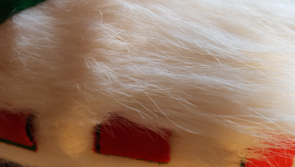 Närbild av vit fluffig päls med röda och gröna detaljer, troligen från en tomteluva eller juldekoration.