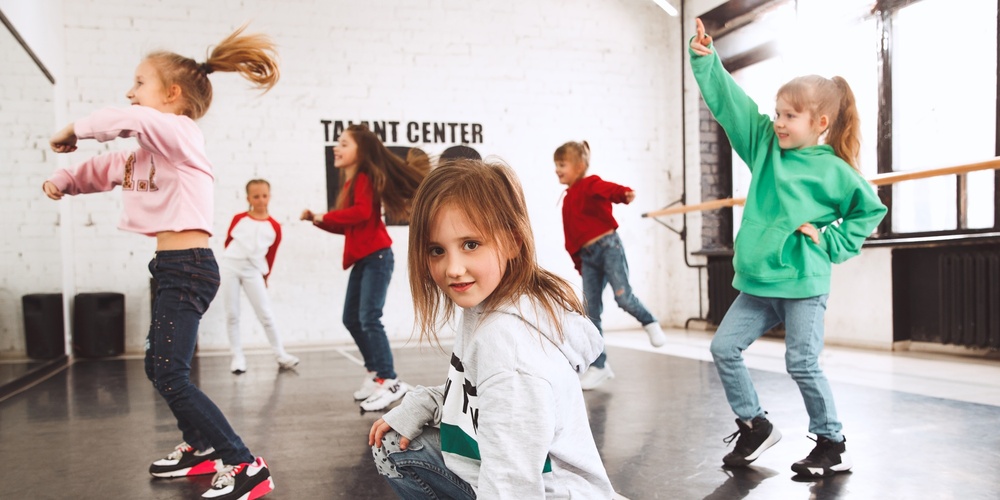 Barn dansar i en ljus dansstudio med stora fönster och spegelvägg.