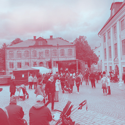 En folksamling på ett torg framför en scen med livemusik, omgiven av gamla stenbyggnader.