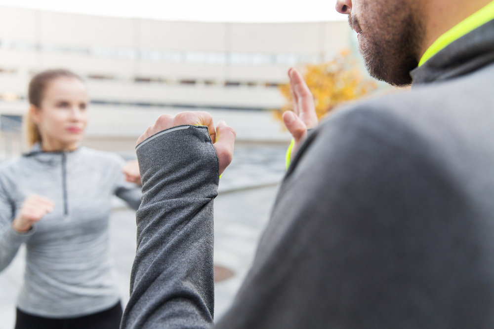 Två personer tränar självförsvar utomhus, båda i grå träningskläder.