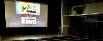 En tom biosalong med rader av stolar och en filmduk som visar en affisch för en filmfestival.