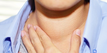 En person håller handen mot sin hals, klädd i blå skjorta, vilket kan tyda på halsont.
