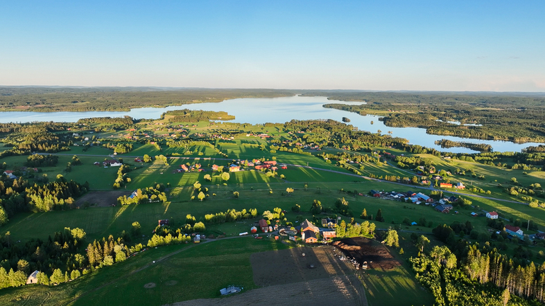 Landskapsvy över gröna fält, gårdar och sjöar under klarblå himmel.