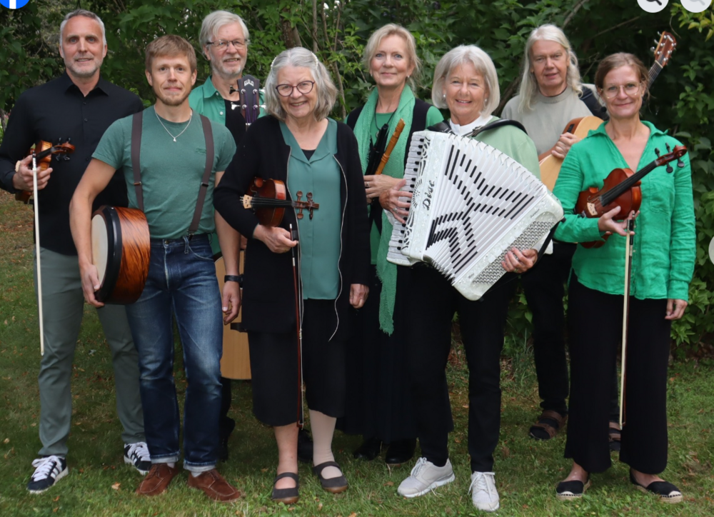 En grupp musiker står utomhus med olika instrument som fiol, dragspel, gitarr och trumma.