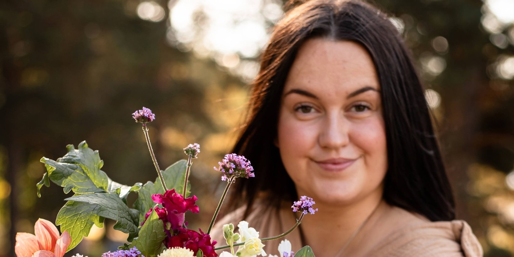 Person håller en stor bukett färgglada blommor utomhus i naturligt ljus.