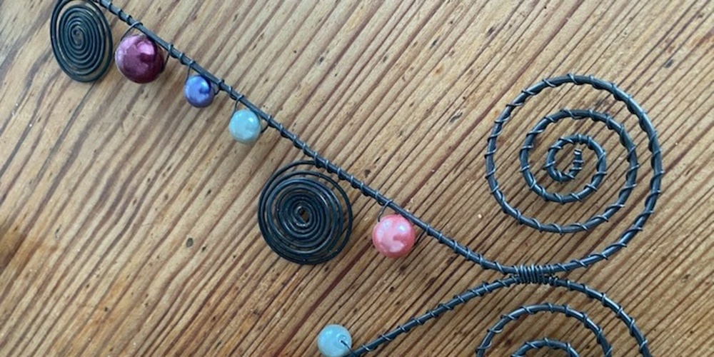 Luffarslöjd dekorativ spiralformad tråd med färgglada pärlor på ett trägolv.