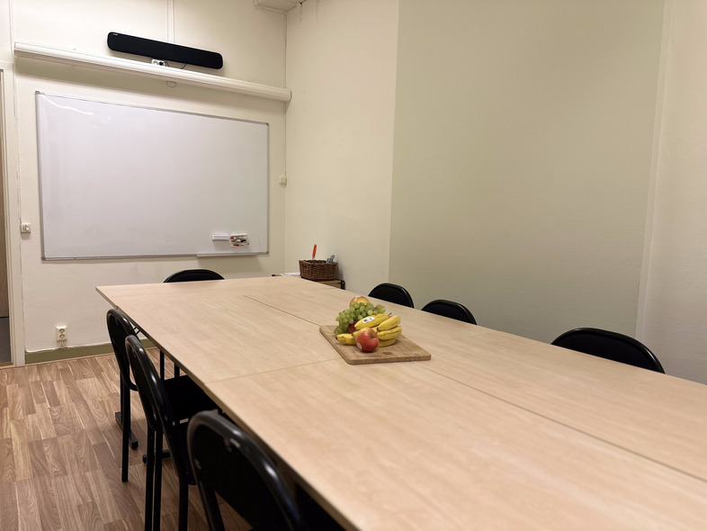 Ett mötesrum med ett långt bord, svarta stolar, en whiteboard och en fruktbricka på bordet.