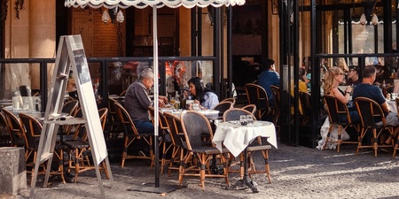 Uteservering på ett parisiskt café med människor som sitter vid bord under en grön markis.