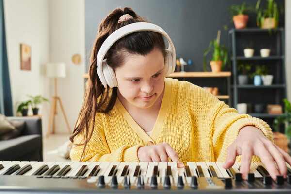 En person i gultröja och hörlurar spelar på en synt.