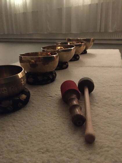Fem tibetanska klangskålar står på rad på en matta med två klubbor framför dem i ett dämpat rum.