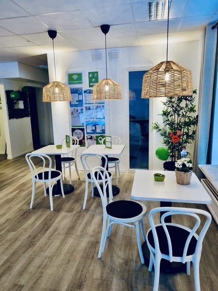 Ljust och modernt café med vita stolar, träbord, växter och flätade lampor i taket.