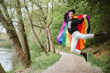 En person hoppar glatt på en skogsstig med en regnbågsflagga svept runt sig.