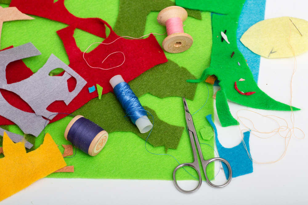 Färgglada tygbitar, trådrullar och en sax på ett bord, material för sömnad eller pyssel.