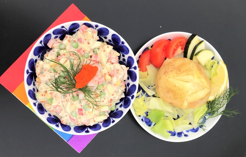 Två tallrikar med mat: en med rysk sallad dekorerad med dill och rom, en med bröd, sallad, tomat och gurka.