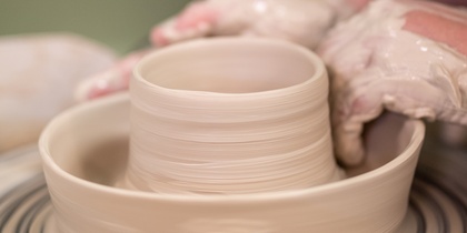 Närbild av händer som formar lera på en drejskiva under keramikarbete.