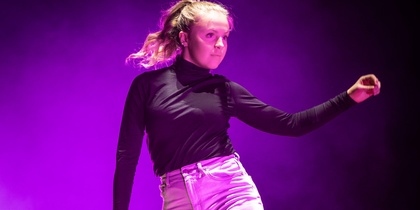 En person dansar barfota på en scen med lila ljus och rökeffekter.