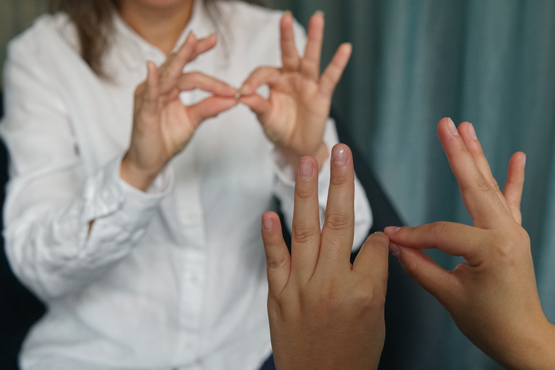 Två personer kommunicerar med teckenspråk, händerna i fokus mot en suddig bakgrund.