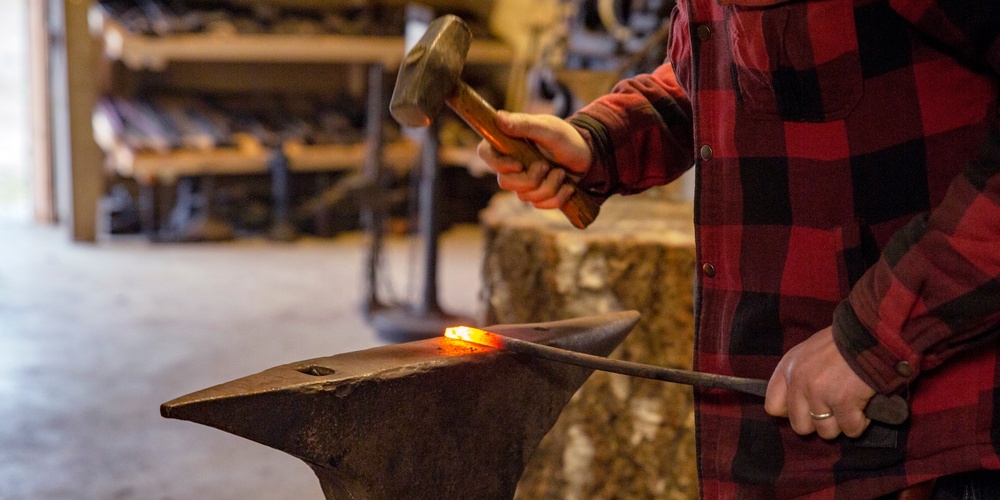 En person smider metall på ett städ med en hammare i en verkstad.