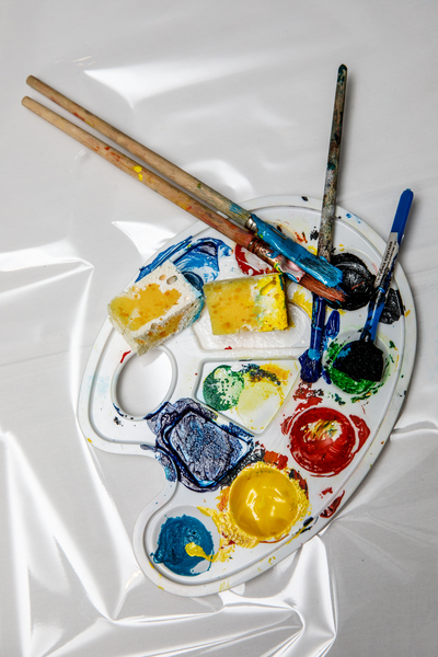 En konstnärspalett med färgglada färger, penslar och svampar på en vit bakgrund.